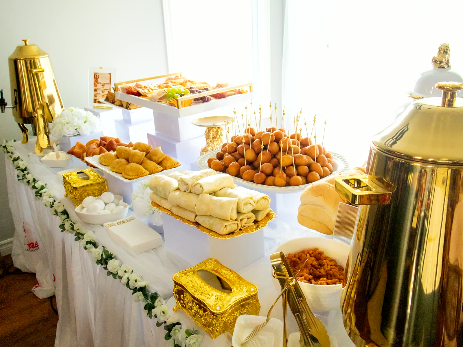 Snack table of samosas, mandazi, spring rolls and pastries on a white and gold display at a Toronto event